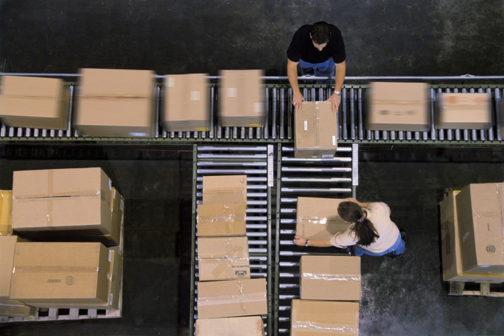 Warehouse employees organizing cardboard boxes moving on a conveyor belt in a distribution